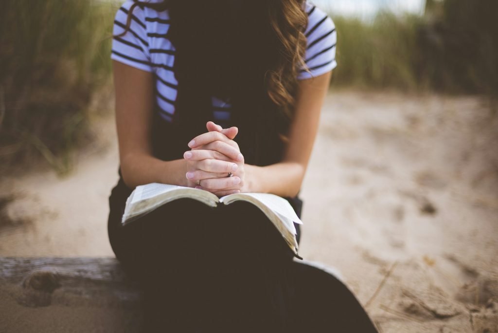 Woman sitting outdoors with hands folded over an open book